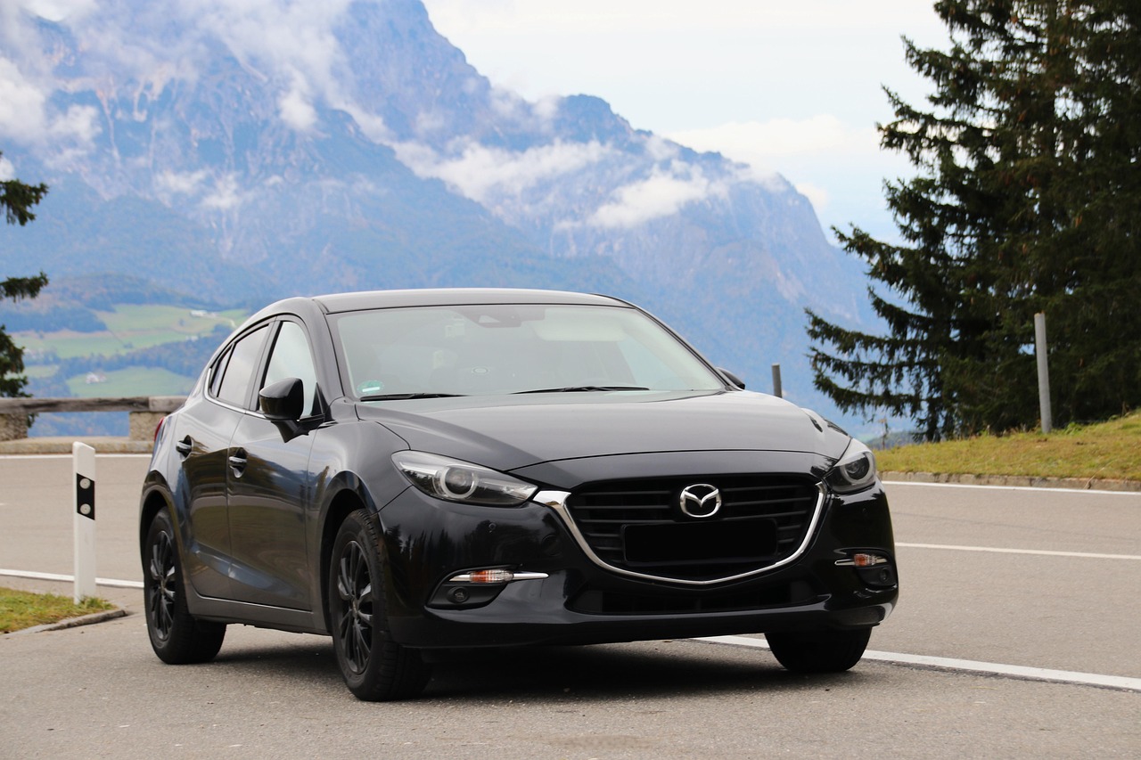 Black Mazda 3 hatchback parked with mountains in the background, showing its wheels and tires.
