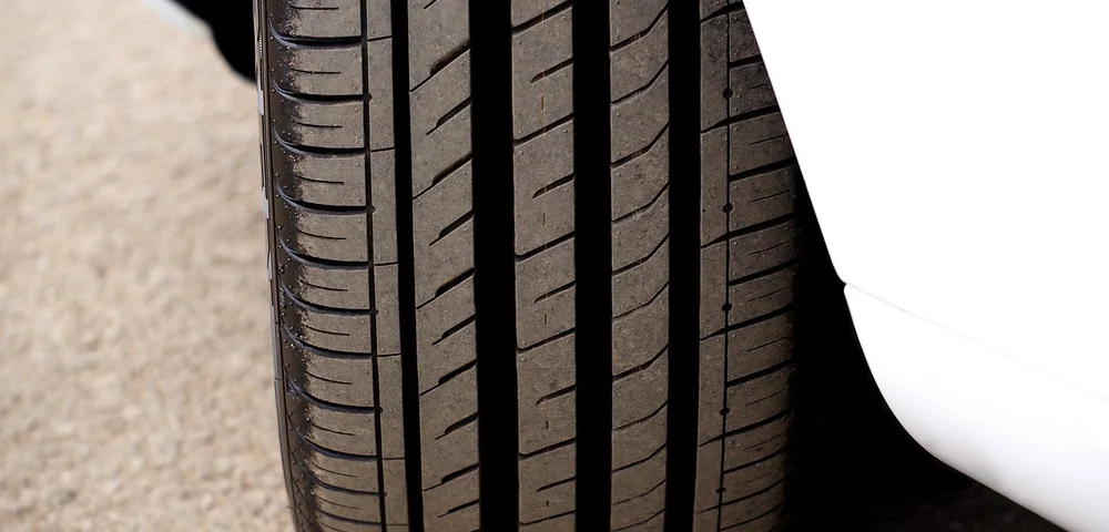 Close-up of a car tire tread against a white vehicle fender on pavement