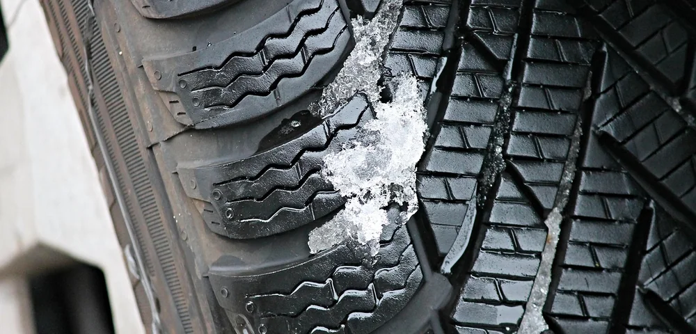 Close-up of a tire's tread pattern showing grooves and siping, with a bit of snow and ice caught in the tread.