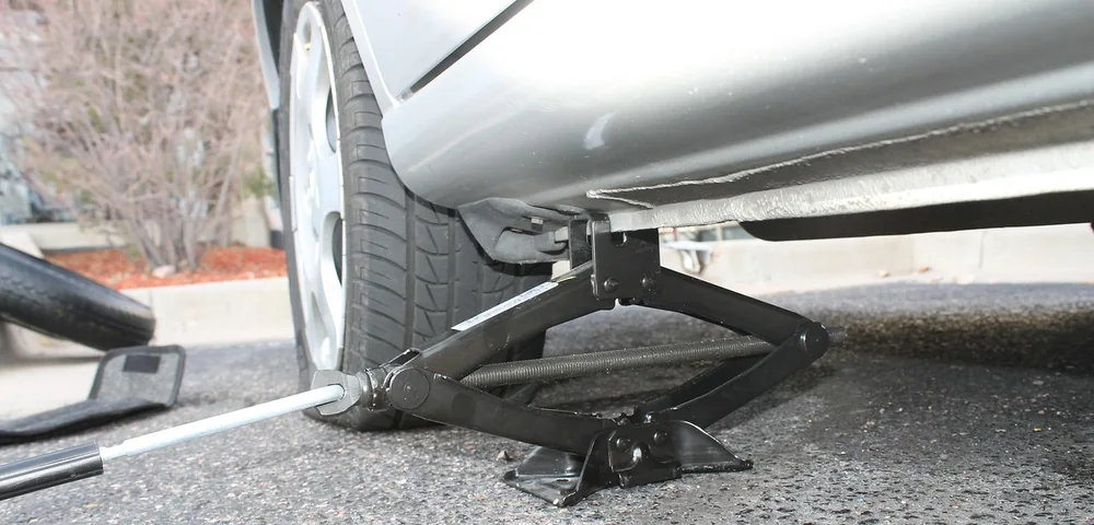 A car tire being raised off the ground by a scissor jack during a tire change