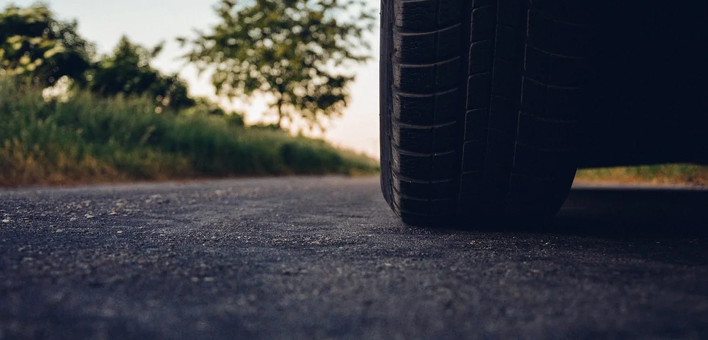 Close-up of a car tire tread on an asphalt road with greenery in the background.