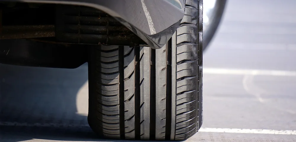 Close-up of a car tire and wheel well showing tread pattern while parked on pavement.