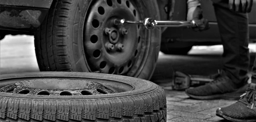 Mechanic changing a light truck tire with a lug wrench, spare tire in foreground
