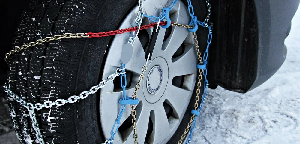 Close-up of a car tire wrapped in snow chains on a snowy road.