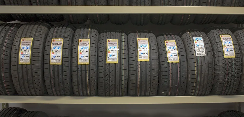 Rows of car tires displayed on shelves with yellow specification labels in a tire shop
