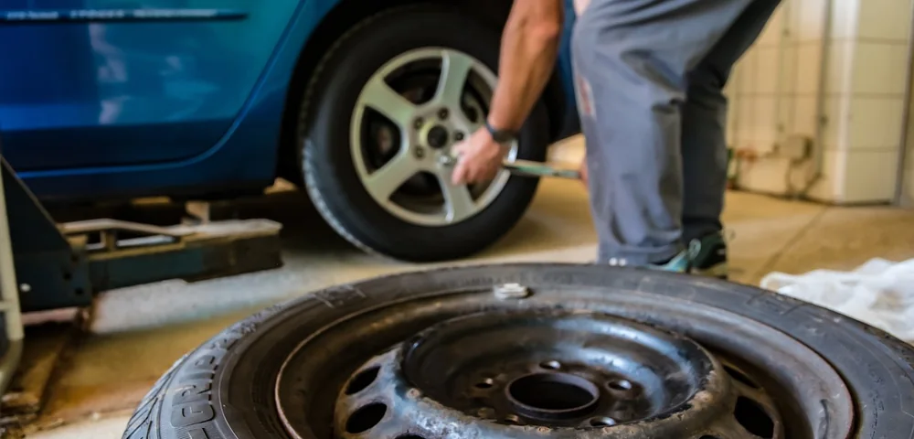 Mechanic changing a car tire, with a used tire's tread pattern visible in the foreground.