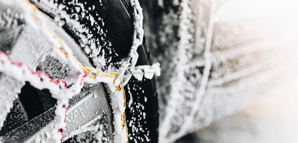 Close-up of a car tire wrapped in snow chains, covered in frost and ice