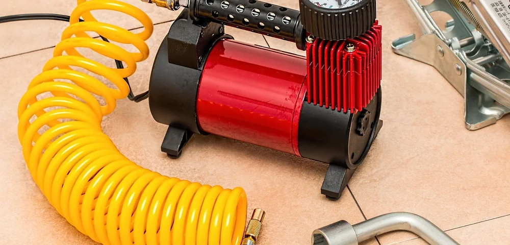 Analog tire pressure gauge mounted on a red and black air compressor with a coiled yellow hose.
